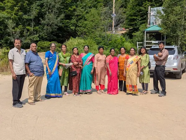 Group, many women in saris, posing outdoors in a parking area