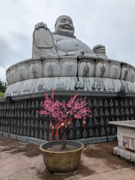 Large white seated Buddha statue with a potted red plant in front