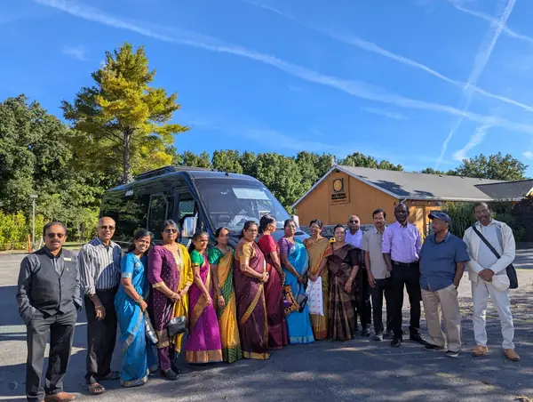 Large group posing in front of a wooden building under a blue sky