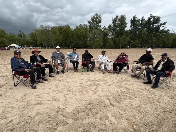 People seated in a circle of chairs on a sandy beach