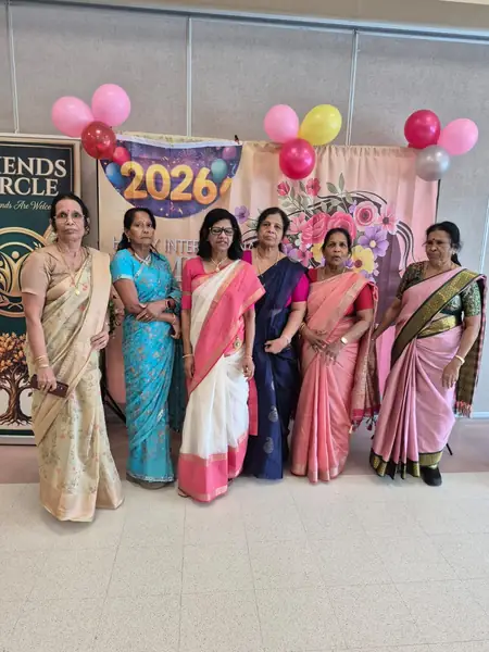 Women in saris posing in front of a backdrop with balloons